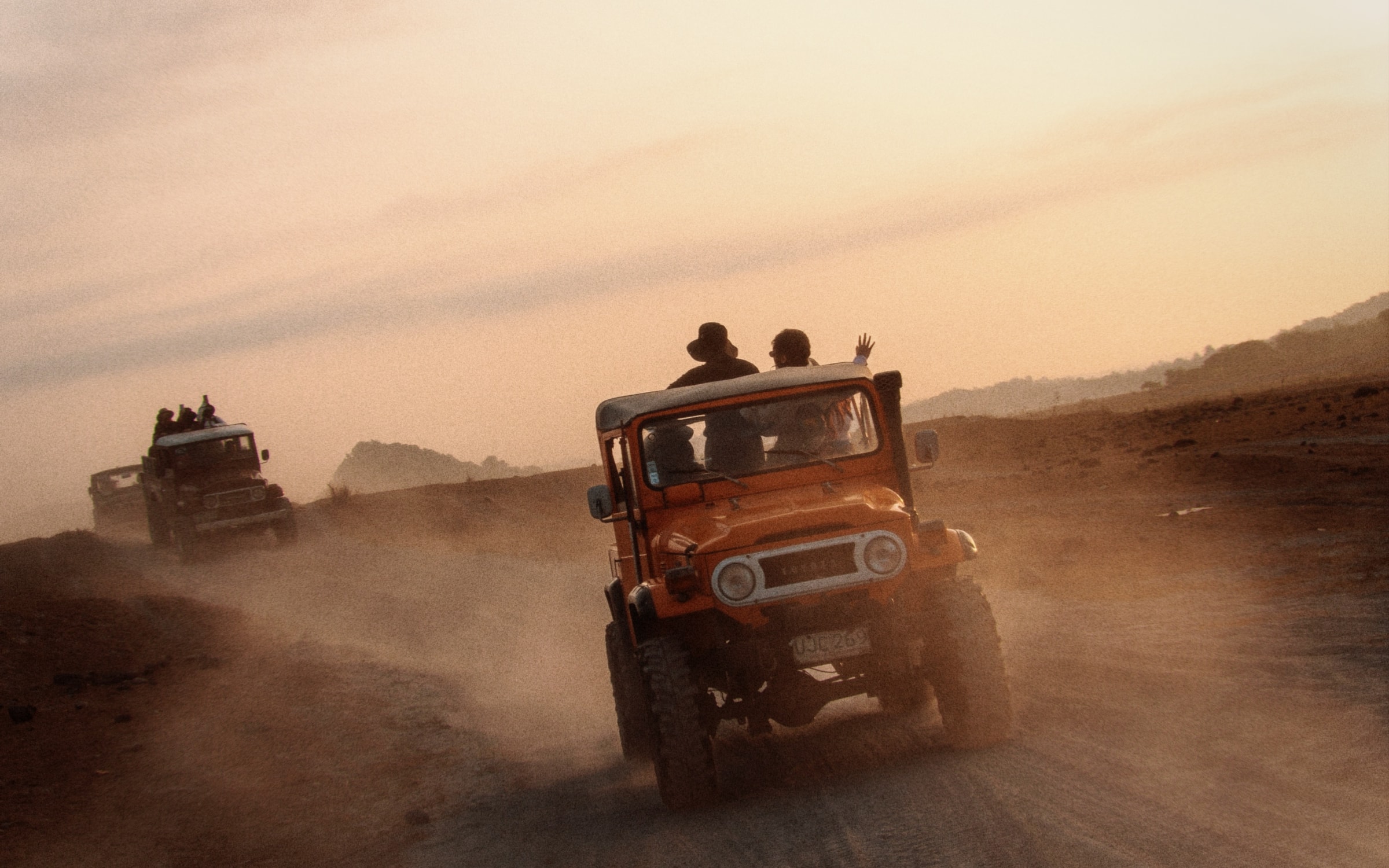 Two jeeps kicking up dust on a desert track under a bright sunset sky