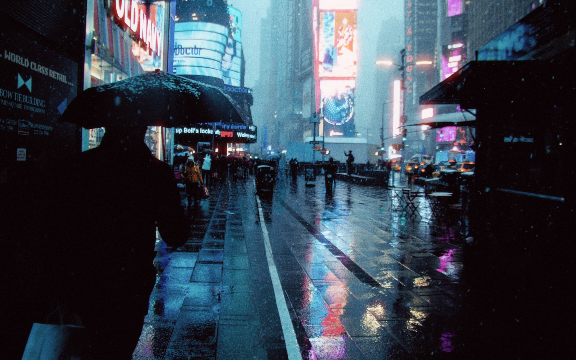 People under umbrellas on a rainy Times Square sidewalk at night, neon reflected on the wet pavement