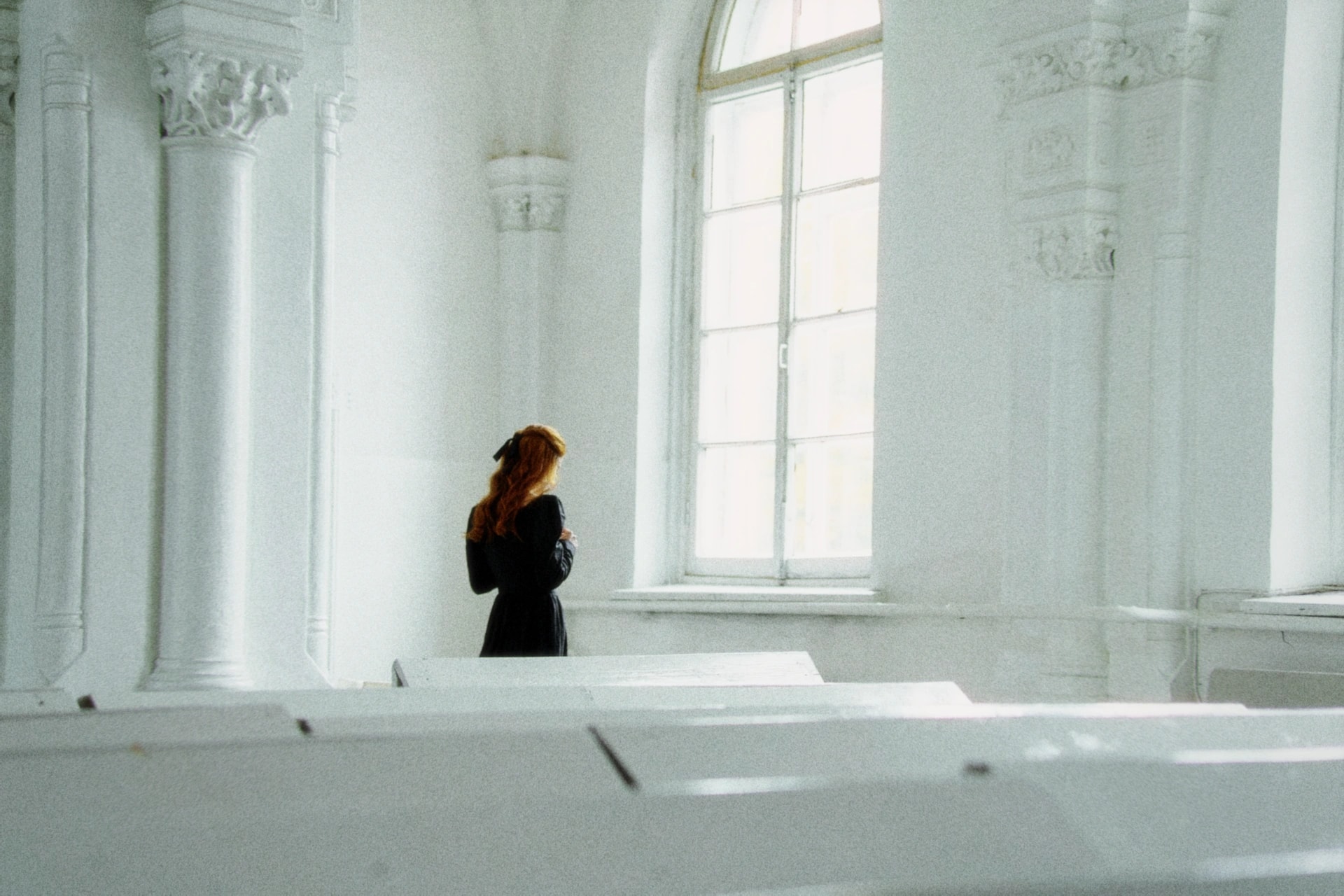 A red-haired woman in a black dress standing in a white hall by a tall window, rendered with the Daydream preset