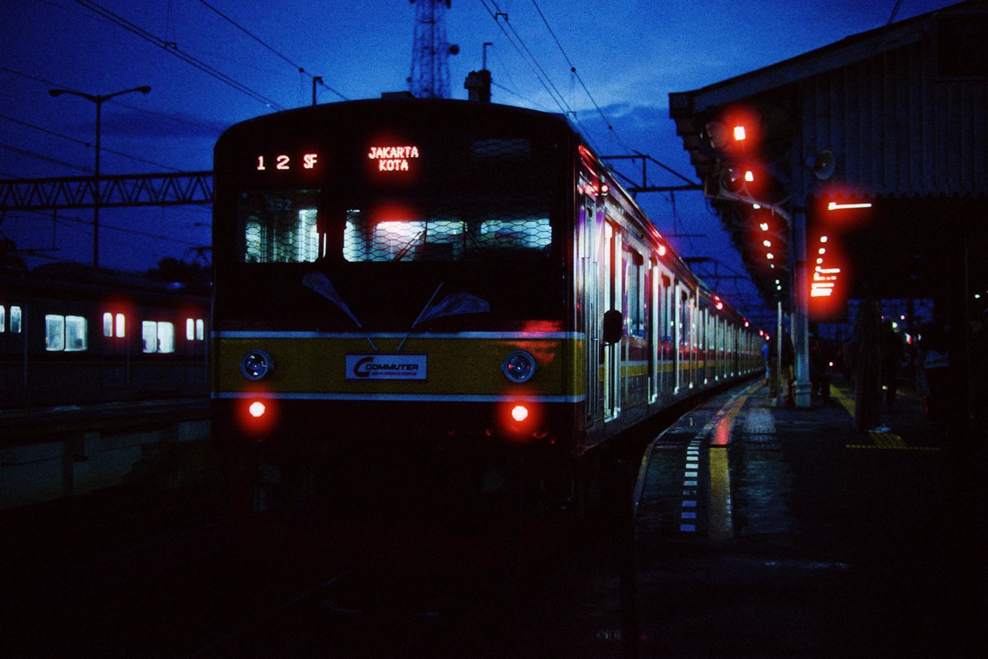 A commuter train standing at a platform at dusk, its headlights on, rendered with the Nightcall preset