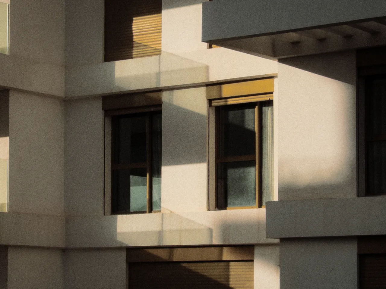 Late sun across a pale apartment facade, its windows half in shadow, with toning at 30%