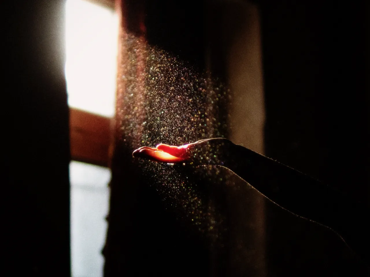 A hand reaching into a dusty beam of window light in a dark room, with temperature at 5500K