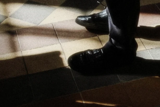 ASA 800 grain, heaviest in the shadows, a close crop of black shoes on a checkered floor crossed by bars of sunlight