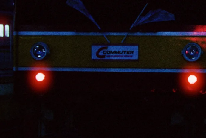 Red halation around the headlights, a close crop of a commuter train standing at a platform at dusk, its headlights on